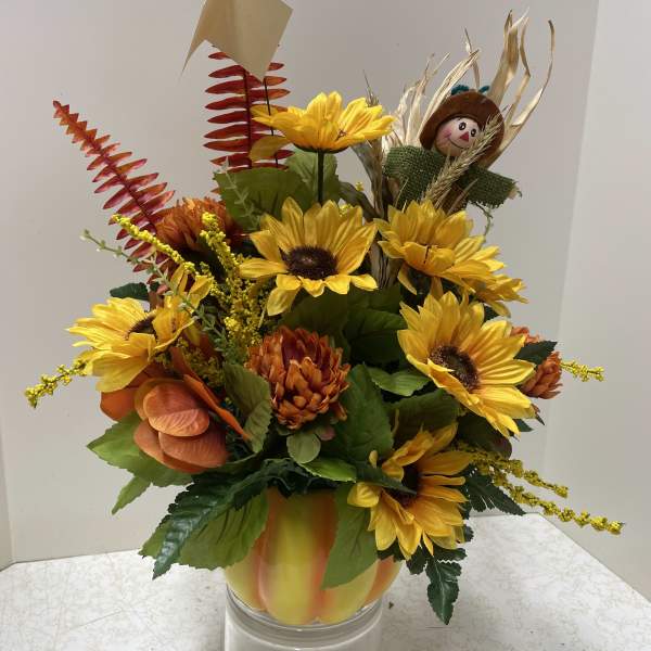 Sunflower arrangement in a clear glass vase with a small scarecrow pick