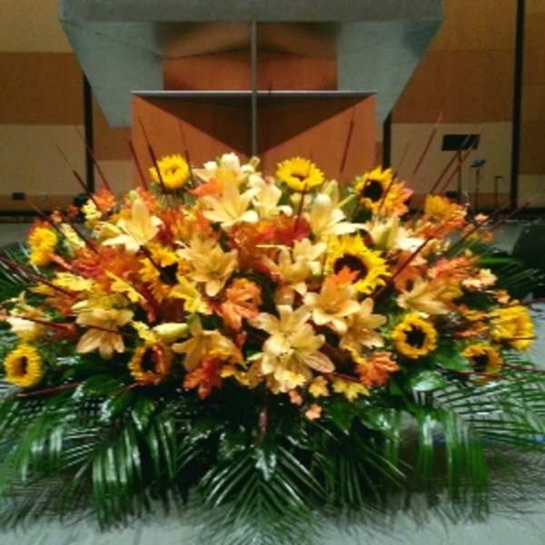Large low altar-style arrangement of yellow lilies and sunflowers with orange blooms and palm fronds