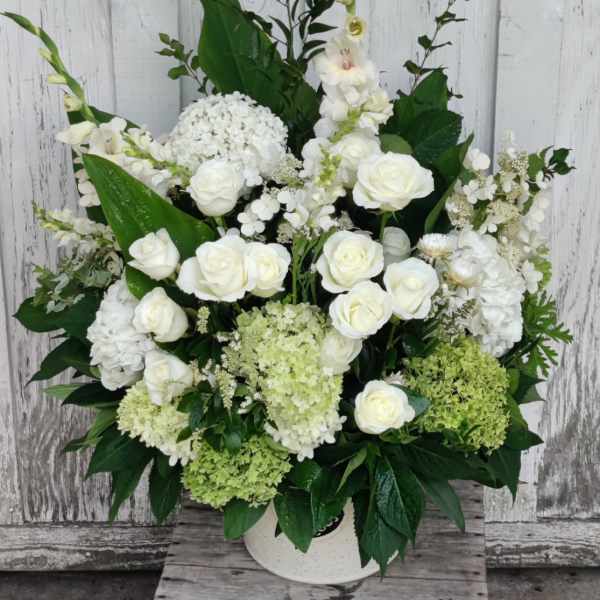 White roses and hydrangeas arranged in a white vase with tall greenery