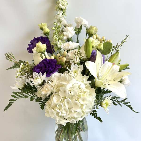 White and purple floral arrangement in a clear glass vase