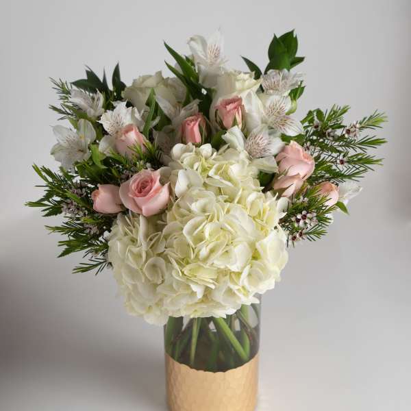White hydrangeas and pink roses in a glass vase with greenery