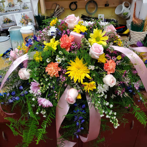Large floral arrangement with pink roses, yellow daisies, and pink ribbons
