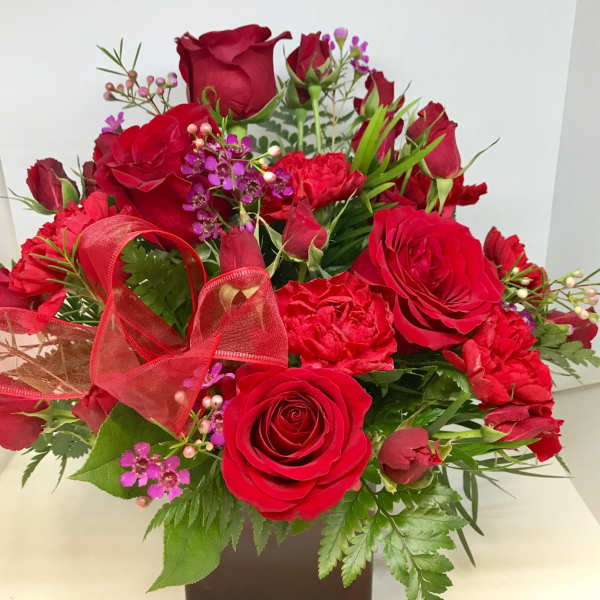 Red roses and carnations in a square vase with a red ribbon