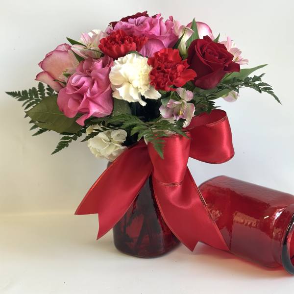 Pink and red bouquet in a red glass vase with a large ribbon