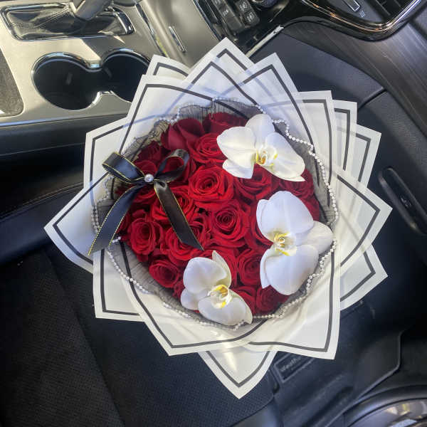 Bouquet of red roses with white orchids and black ribbon in a car seat