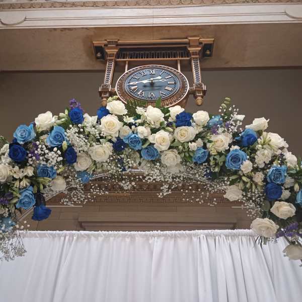Large floral arch of blue and white roses beneath a wall clock