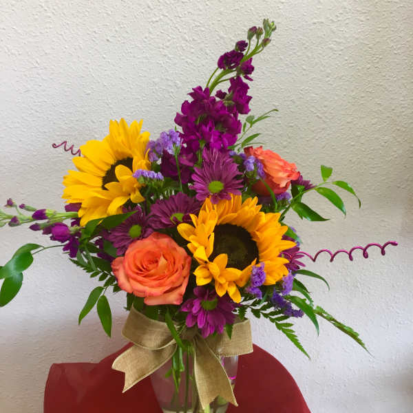 Bouquet of sunflowers, purple blooms, and orange roses in a glass vase