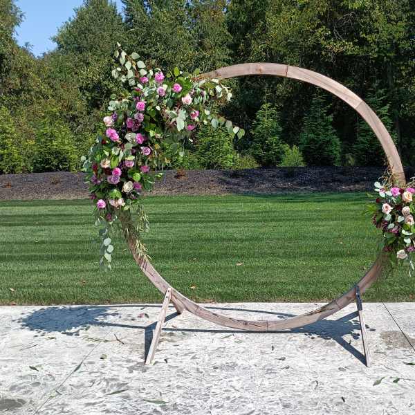Floral-decorated wooden circle arch with pink and white flowers outdoors