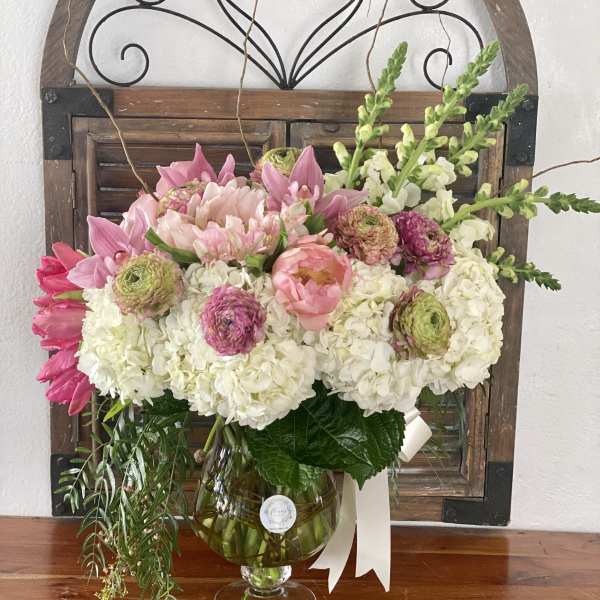 Pink and white floral arrangement in a glass vase with a ribbon