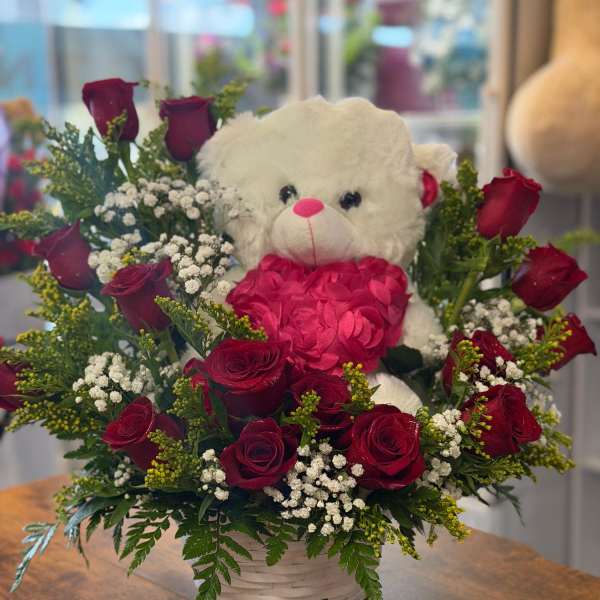 White teddy bear surrounded by red roses in a basket