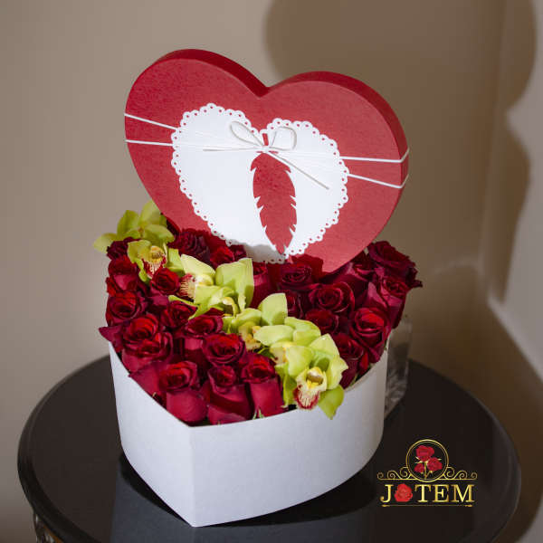Heart-shaped box of red roses with pale green orchids and a heart topper