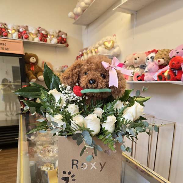 White roses and greenery in a gift box with a teddy bear on top