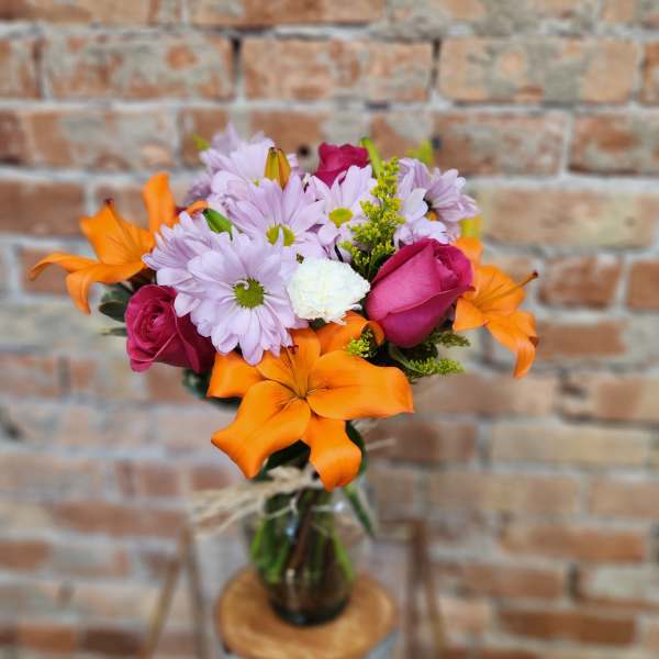 Bouquet of orange lilies, pink roses, and lavender daisies in a glass vase