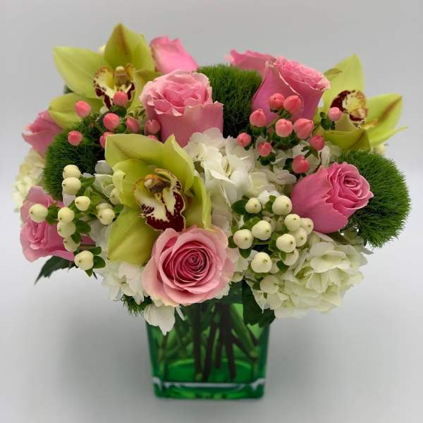 Pink roses and green orchids arranged in a green glass vase
