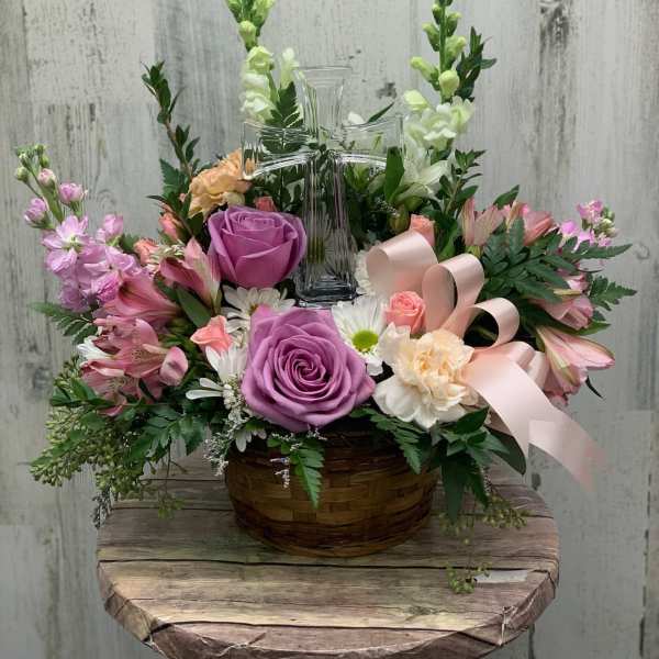 Basket arrangement with pink and purple flowers around a clear glass cross