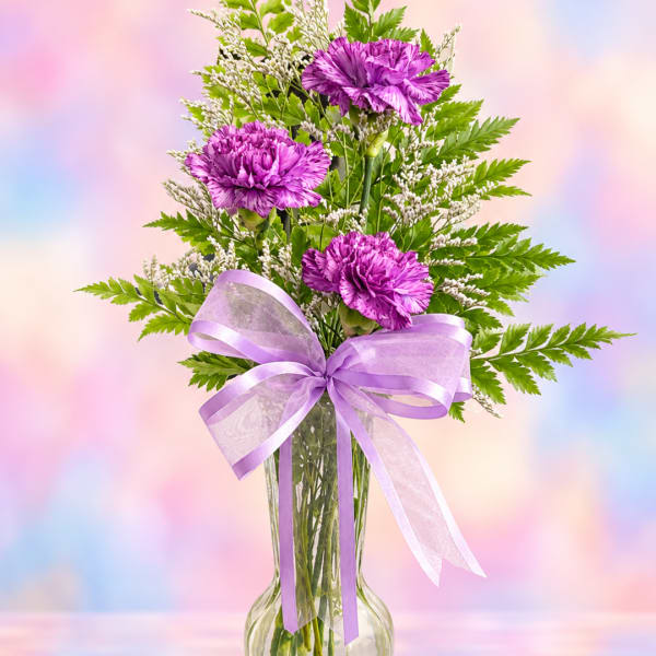 Purple carnations in a clear vase with a lavender ribbon bow
