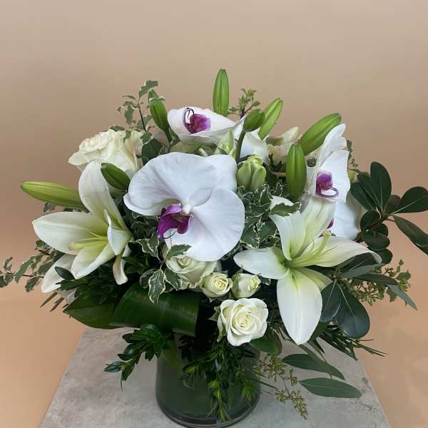 White lilies and orchids arranged in a green glass vase