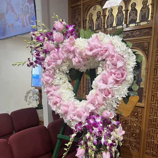 Heart-shaped floral wreath with pink roses and white flowers on an easel
