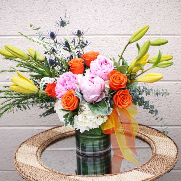 Bouquet of orange roses, pink blooms, and yellow lilies in a glass vase