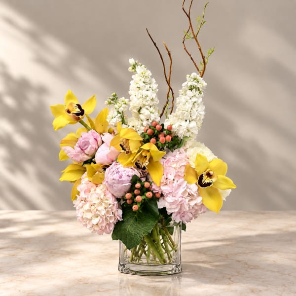 Mixed bouquet of yellow orchids, pink hydrangeas, and white flowers in a glass vase