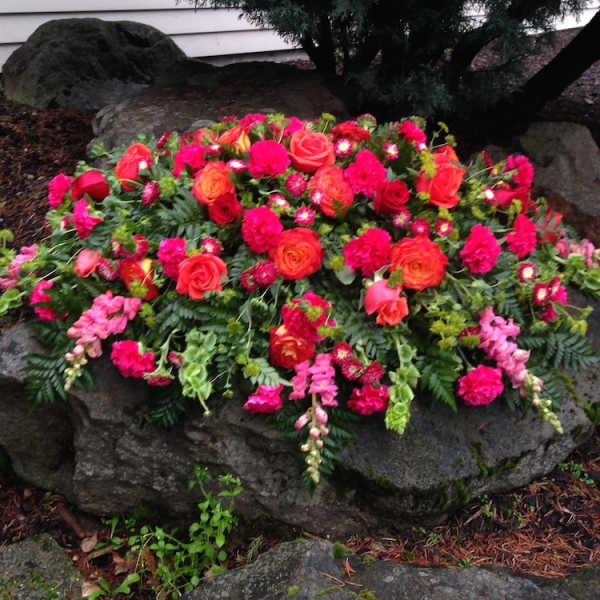 Bright pink and orange floral arrangement on a large rock