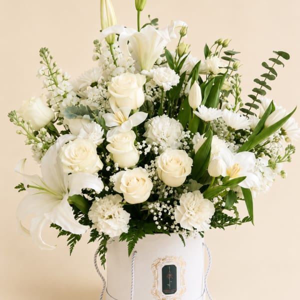 White floral arrangement in a white hatbox with lilies and roses