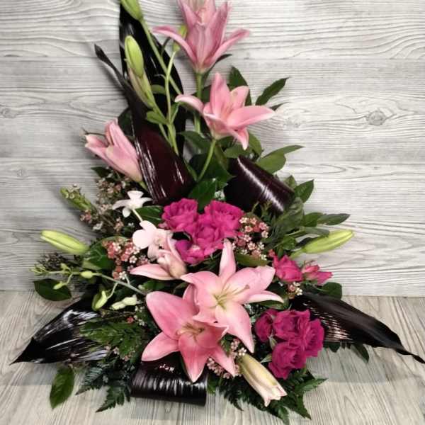 Pink lilies and magenta flowers in a low arrangement with dark leaves