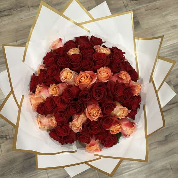 Bouquet of red and peach roses wrapped in white paper with gold trim
