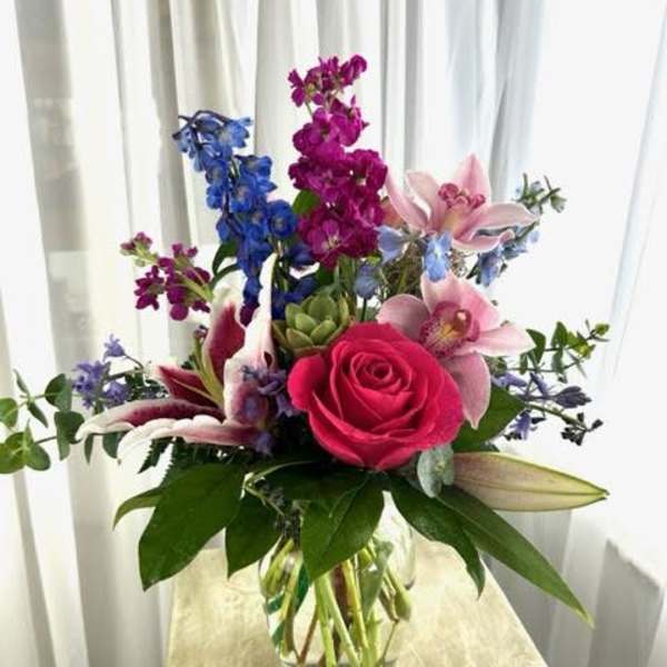 Mixed bouquet with pink rose, lilies, and blue-purple flowers in a glass vase