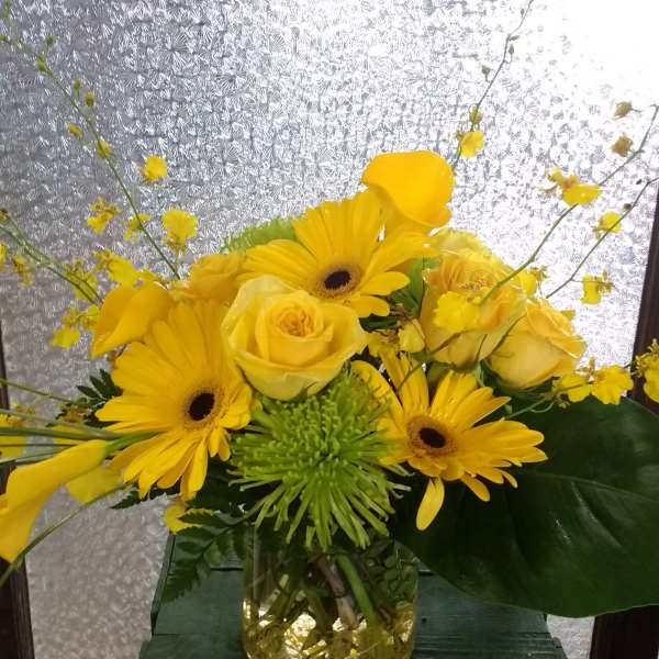 Yellow roses and gerbera daisies arranged in a glass vase