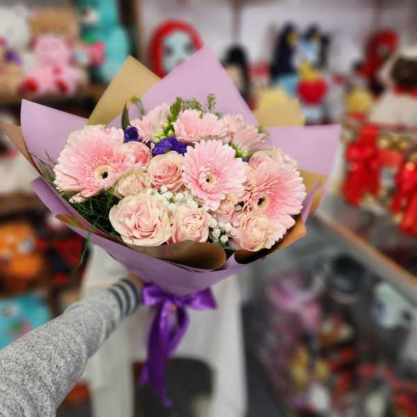 Bouquet of pink gerbera daisies and roses wrapped in purple paper