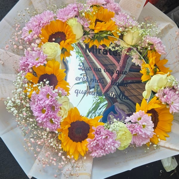 Circular bouquet with sunflowers, pale roses, and pink daisies around a mirror