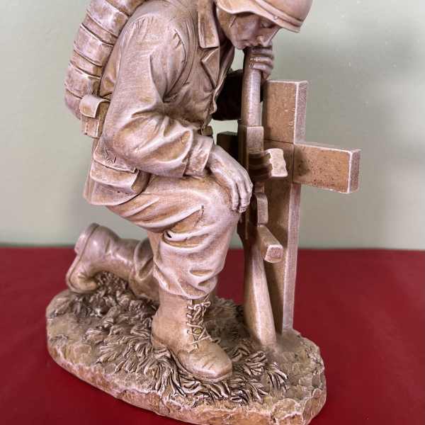 Stone soldier kneeling beside a cross memorial statue