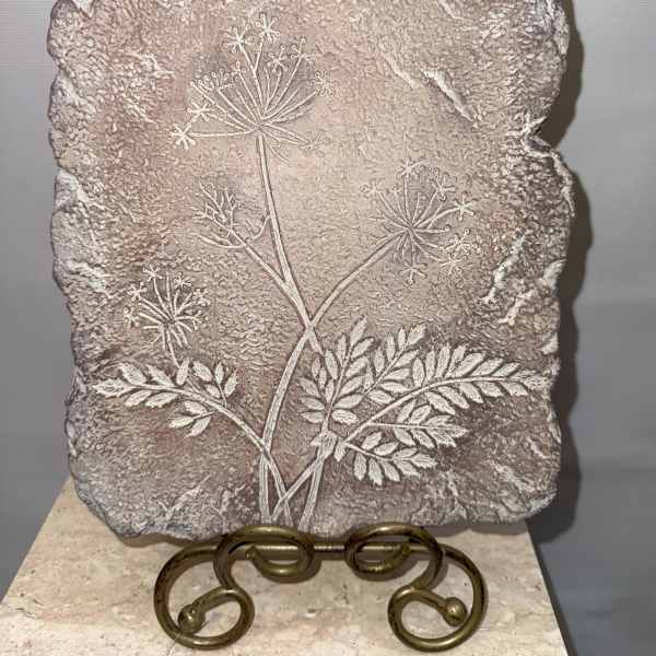 Textured stone plaque with an etched floral stem design on a metal stand
