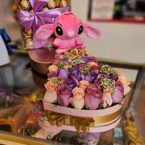 Pink plush toy atop a rose arrangement with a chocolate box behind it