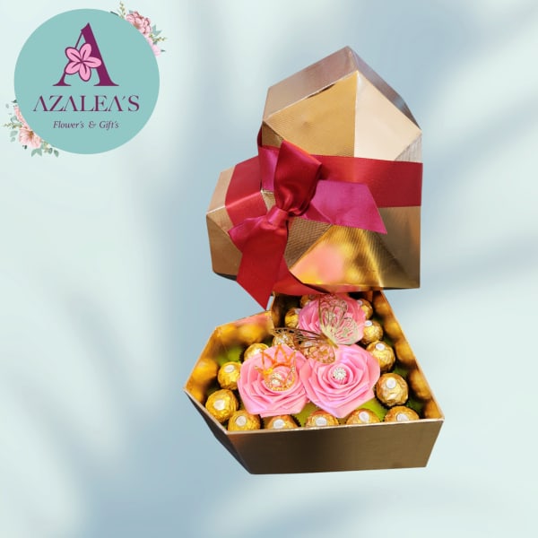 Pink rose decorations in a gold gift box with chocolates and a red ribbon