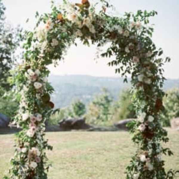 Floral arch covered in white and blush flowers with greenery outdoors