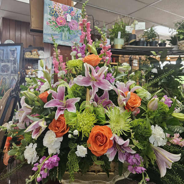 Large basket arrangement with pink lilies, orange roses, green mums, and white carnations on a small stand