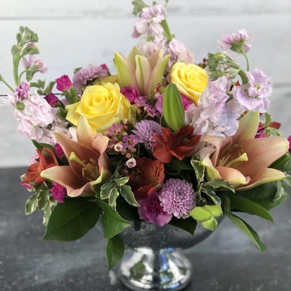 Mixed bouquet of yellow roses, lilies, and pink flowers in a silver vase