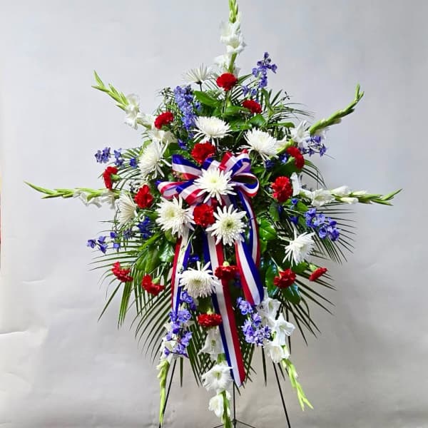 Standing floral spray with white, red, and blue flowers and a ribbon bow