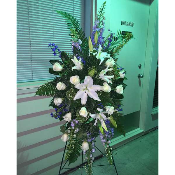 Tall standing floral spray with white lilies and purple flowers on an easel