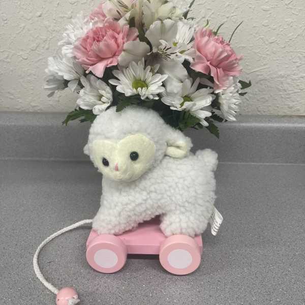Plush lamb toy with a pink wheeled base and a bouquet of pink and white flowers