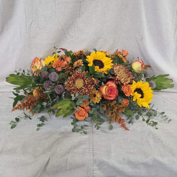 Low autumn centerpiece with sunflowers, orange roses, and bronze mums in a long oval design