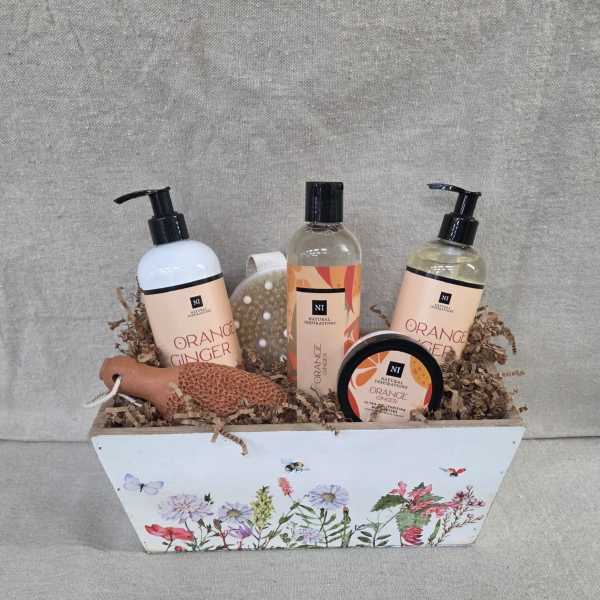 Bath gift set with orange ginger products in a floral-printed white wooden box filled with paper shred.