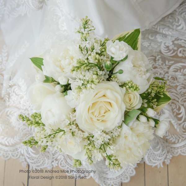 White bridal bouquet with roses and peonies on lace fabric