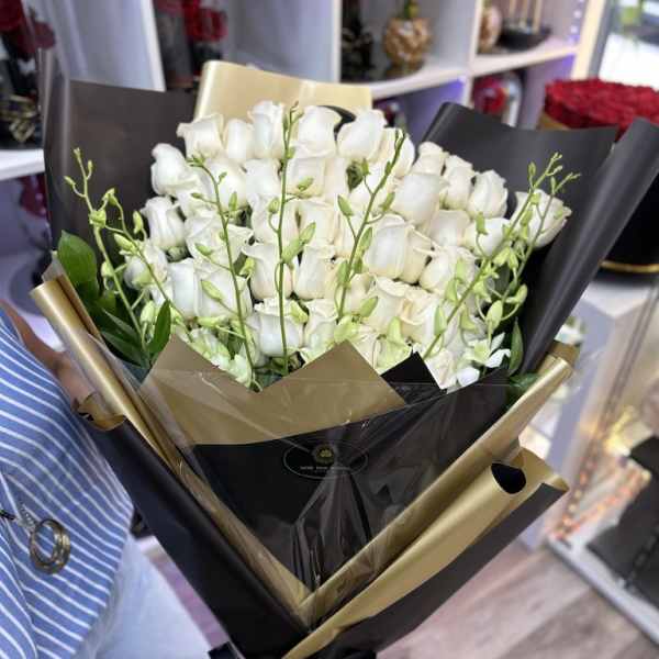Tall bouquet of white roses with green orchid buds wrapped in black and gold paper