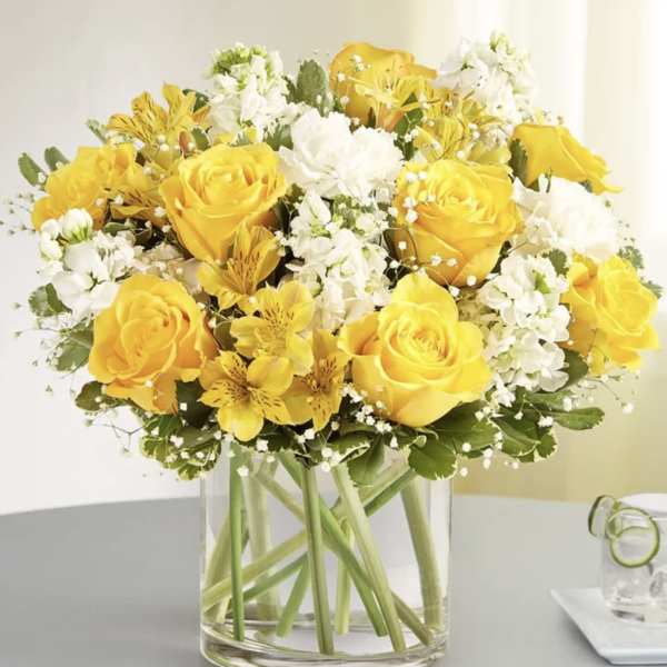 Yellow roses and white flowers arranged in a clear glass vase