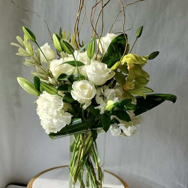 Tall arrangement of white roses, lilies, hydrangeas, and green orchids in a clear glass vase