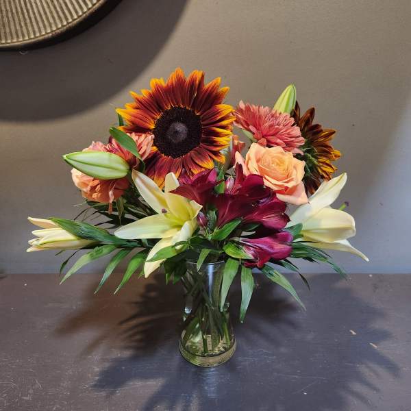 Mixed bouquet with sunflowers, lilies, roses, and pink blooms in a glass vase