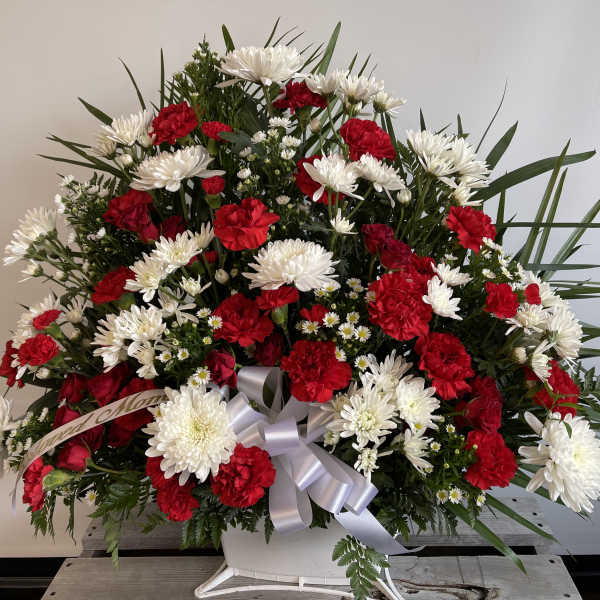 Red carnations and white daisies in a white container with a silver ribbon